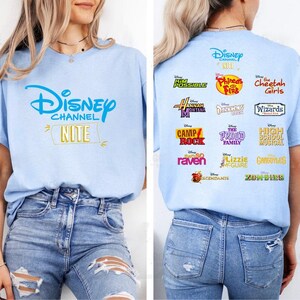 May include: Light blue t-shirt featuring the Disney Channel logo and the word "Nite" in gold. The back of the shirt displays logos from various Disney Channel shows, including "Kim Possible," "Hannah Montana," and "High School Musical."