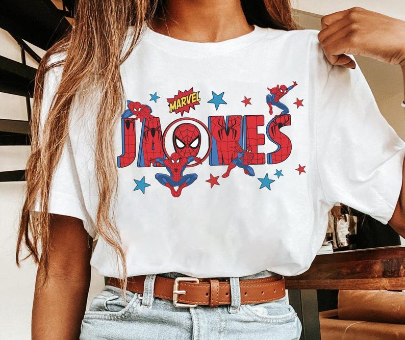 May include: White t-shirt featuring a colorful graphic of Spider-Man and the name "JONES" in red and blue block letters. The Marvel logo is above the name, with stars scattered around the design.