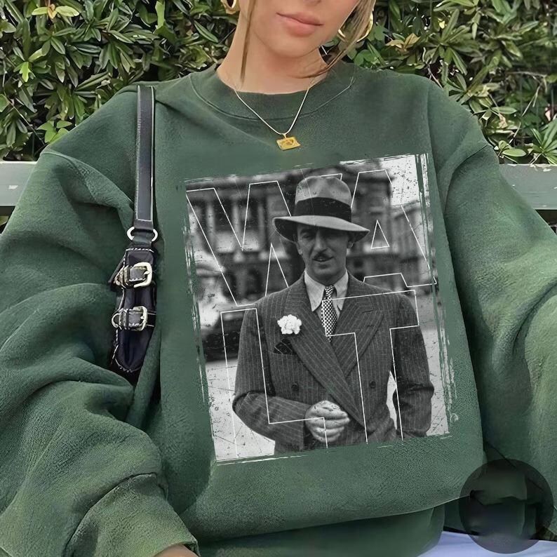 May include: Dark green sweatshirt with a black and white image of a man in a suit and hat. The image is framed with white lines. The sweatshirt has a crew neck and long sleeves. A black purse with silver hardware hangs from the shoulder.