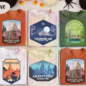 Puede incluir: Seis camisetas de diferentes colores, incluyendo naranja, blanco y verde. Cada camiseta presenta un dise&ntilde;o gr&aacute;fico diferente, incluyendo los textos "Fantasyland", "Tomorrowland", "Adventureland", "Frontierland" y "Galaxy's Edge".