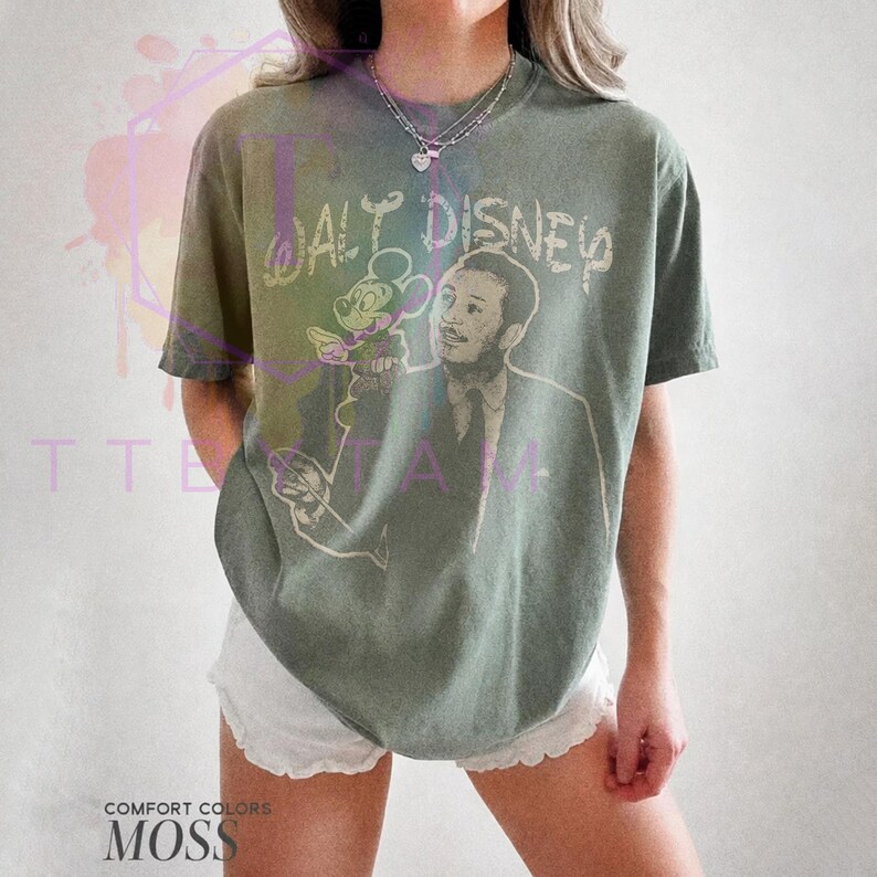 Może przedstawiać: Koszulka z kr&oacute;tkim rękawem w kolorze mchu z nadrukiem graficznym przedstawiającym Walta Disneya i Myszkę Miki. Napis "WALT DISNEY" jest nadrukowany jasną czcionką nad ilustracją. Koszulka ma okrągły dekolt i luźny kr&oacute;j.