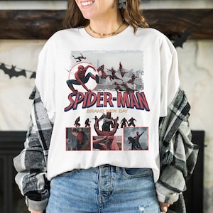 May include: White t-shirt featuring a Spider-Man graphic. The design includes the words "SPIDER-MAN" in red and blue, with additional imagery of the superhero in action. The phrase "BRAND NEW DAY" is also present.