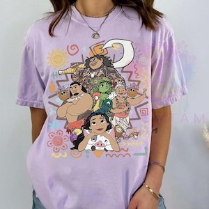 May include: A lilac-colored t-shirt featuring a colorful graphic of characters from a popular animated movie. The design includes various figures, a sun, and decorative patterns. The shirt has short sleeves and a relaxed fit, perfect for casual wear.