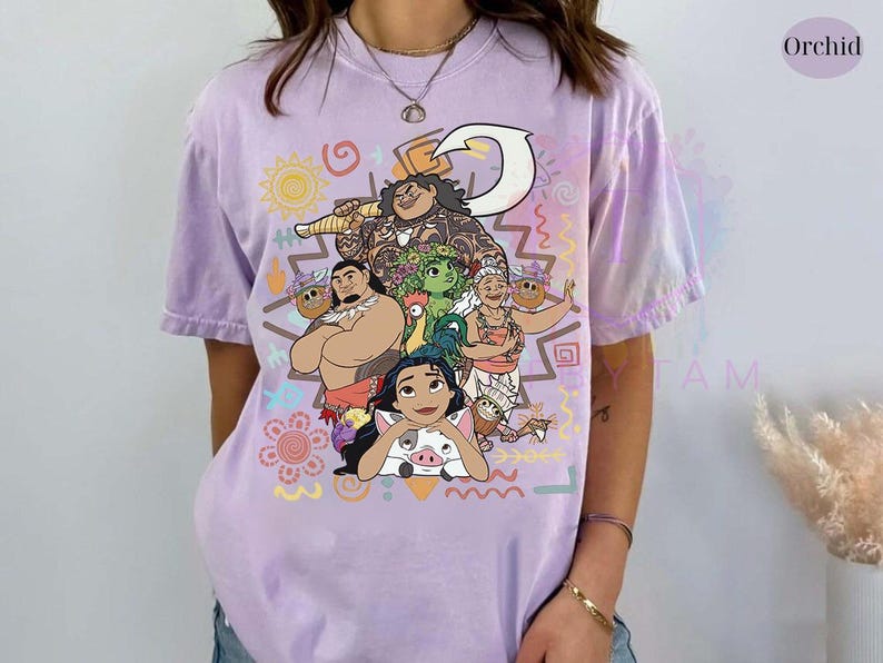 May include: A lilac-colored t-shirt featuring a colorful graphic of characters from a popular animated movie. The design includes various figures, a sun, and decorative patterns. The shirt has short sleeves and a relaxed fit, perfect for casual wear.