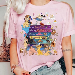 Puede incluir: Camiseta rosa con un dise&ntilde;o que presenta t&iacute;tulos y personajes de pel&iacute;culas de Disney. El dise&ntilde;o incluye personajes de "La Bella y la Bestia", "Aladd&iacute;n", "101 D&aacute;lmatas", "Pocahontas" y "El Rey Le&oacute;n". La camiseta tiene cuello redondo y mangas cortas.