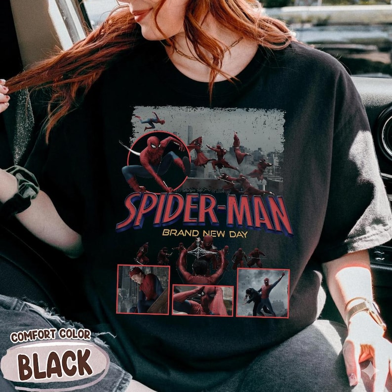 May include: Black t-shirt featuring a Spider-Man graphic. The design includes the words "SPIDER-MAN BRAND NEW DAY" in red and blue, with images of Spider-Man in action. The shirt also has the words "COMFORT COLOR BLACK" printed on it.