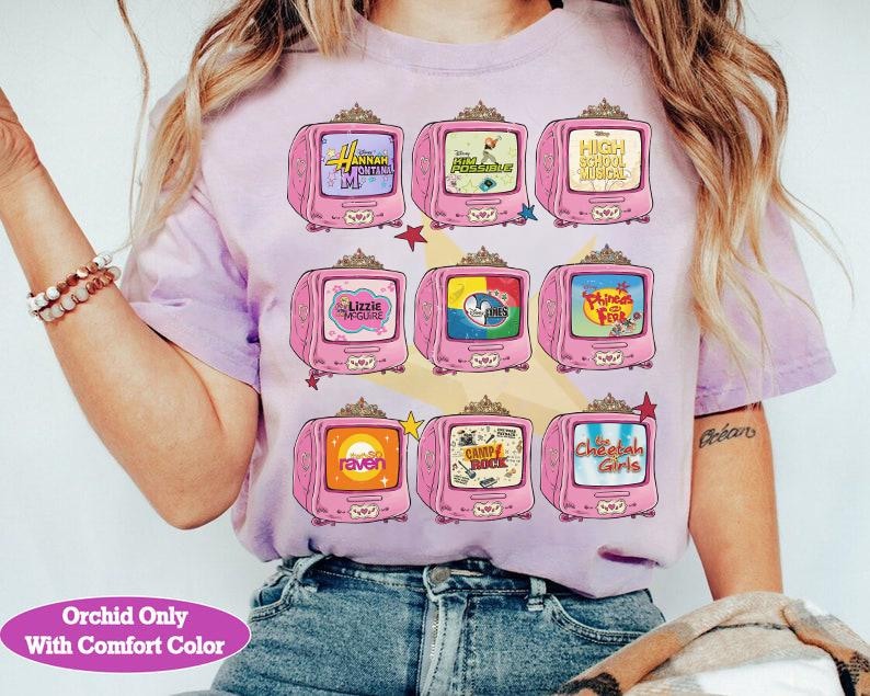 May include: A light purple t-shirt featuring a design of nine pink retro televisions. Each TV screen displays a different show title, including "Hannah Montana," "High School Musical," and "The Cheetah Girls." The text "Orchid Only With Comfort Color" is at the bottom.