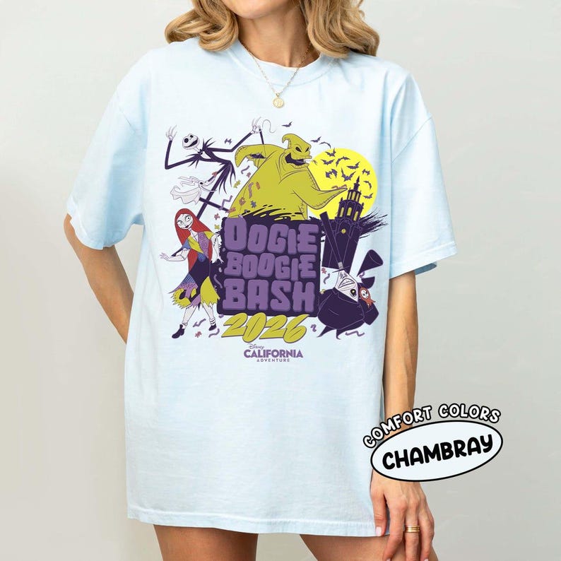 May include: Light blue t-shirt featuring a graphic design for the "Oogie Boogie Bash 2026" event. The design includes characters like Jack Skellington, Sally, and Oogie Boogie, with the text "Disney California Adventure". The shirt is labeled "Comfort Colors Chambray".