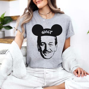 Puede incluir: Camiseta gris con un gr&aacute;fico en blanco y negro de Walt Disney con orejas de Mickey Mouse, con el nombre "WALT" impreso. La camiseta es de cuello redondo.