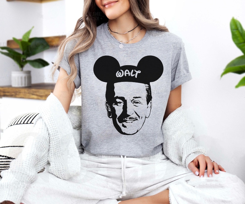 Puede incluir: Camiseta gris con un gr&aacute;fico en blanco y negro de Walt Disney con orejas de Mickey Mouse, con el nombre "WALT" impreso. La camiseta es de cuello redondo.
