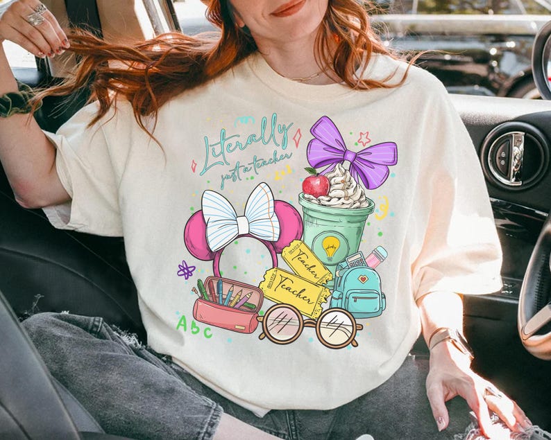 May include: Cream-colored t-shirt with a colorful graphic that reads "Literally just a teacher." The design includes a pink Minnie Mouse bow, a green coffee cup with whipped cream, a red apple, and school-themed elements.