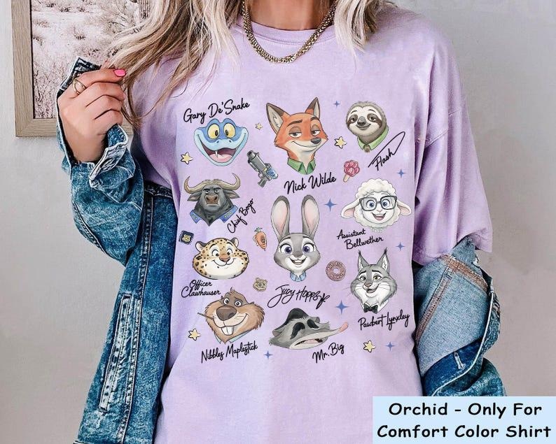 K&ouml;nnte beinhalten: Orchideenfarbenes Comfort Color-Shirt mit Illustrationen von Zeichentrickfiguren aus Zootopia, darunter Judy Hopps, Nick Wilde und Flash. Der Text "Orchid - Only For Comfort Color Shirt" befindet sich unten.