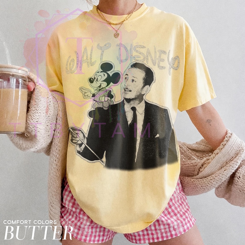 Może przedstawiać: Bladoż&oacute;łty t-shirt z kr&oacute;tkim rękawem z czarno-białym nadrukiem graficznym przedstawiającym Walta Disneya i Myszkę Miki. Napis "WALT DISNEY" jest wydrukowany stylizowaną czcionką nad postaciami. Koszulka ma okrągły dekolt.