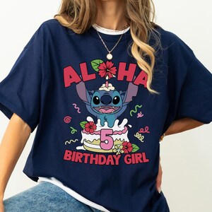 May include: Navy blue t-shirt featuring a graphic of Stitch from Lilo & Stitch. The design includes the word "Aloha", a birthday cake with the number "5", and the text "Birthday Girl". The shirt has short sleeves.