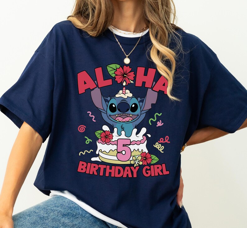 May include: Navy blue t-shirt featuring a graphic of Stitch from Lilo & Stitch. The design includes the word "Aloha", a birthday cake with the number "5", and the text "Birthday Girl". The shirt has short sleeves.