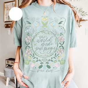 Pu&ograve; includere: T-shirt verde chiaro con un design floreale e la scritta "the world needs your magic". Il design include fiori, foglie e le parole "faith" e "trust". Sono incluse anche le parole "pixie dust".