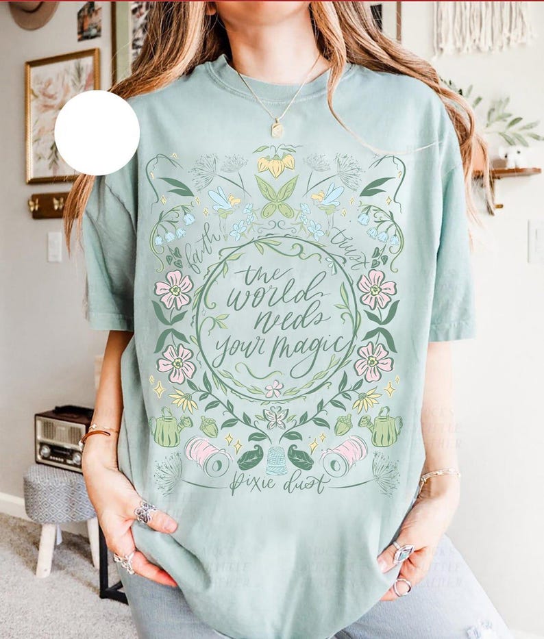 Pu&ograve; includere: T-shirt verde chiaro con un design floreale e la scritta "the world needs your magic". Il design include fiori, foglie e le parole "faith" e "trust". Sono incluse anche le parole "pixie dust".