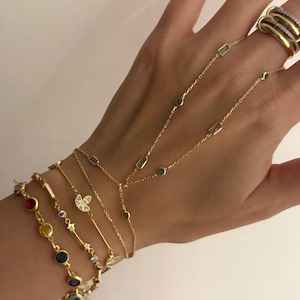 May include: A collection of gold-toned bracelets and a ring. The bracelets feature various designs, including colorful gemstones, delicate chains, and a butterfly motif. The ring has multiple bands with a gold and silver finish.