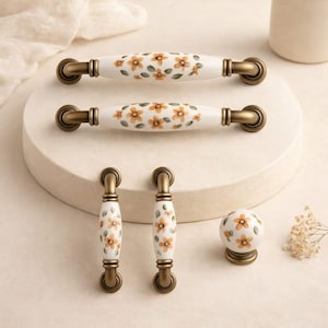May include: A collection of ceramic cabinet hardware featuring a floral design. The set includes two long pulls, two smaller pulls, and a round knob. The hardware has a white base with orange and green floral patterns and bronze-colored metal accents.