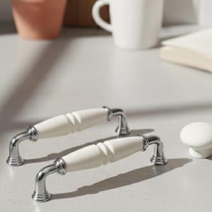 May include: Two white and silver cabinet pulls and a matching knob. The pulls have a curved design with a white, ridged center and silver accents. The knob is a simple, round design with a white finish.