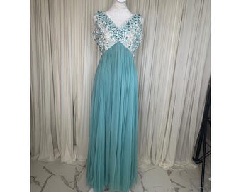 May include: A floor-length sleeveless gown in a muted teal color featuring a V-neckline. The bodice is heavily embellished with silver-toned beads and clear crystals. The skirt is made of a pleated, flowing fabric that falls from the waistline.