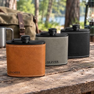 May include: Three rectangular metal flasks with black screw-top caps and black metal trim. The flasks are wrapped in tan, grey, and black textured material with white stitching. The names JAMES, OLIVER, and NOAH are engraved on the front.