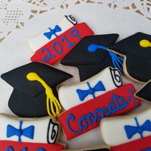 May include: A set of six graduation cookies decorated with red, white, and blue icing. The cookies feature a graduation cap, a diploma, and the year 2019. One cookie says "Congrats!" in blue icing.