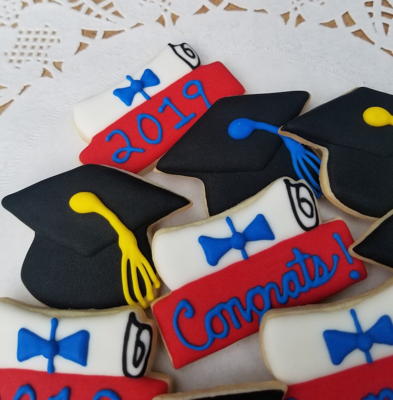 May include: A set of six graduation cookies decorated with red, white, and blue icing. The cookies feature a graduation cap, a diploma, and the year 2019. One cookie says "Congrats!" in blue icing.