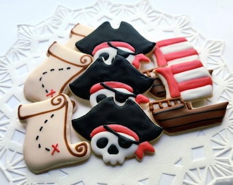 May include: A collection of pirate-themed cookies, including pirate hats, skull faces with eye patches, treasure maps, and a ship with red and white striped sails. The cookies are decorated with black, red, white, and brown icing.