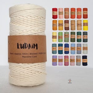 May include: A large spool of off-white braided macrame cord with a brown paper label reading EUDAIM 3mm | Approx. 100m | Braided | 100% Cotton Macrame Cord. To the right, a grid displays 42 smaller spools of the same cord in various solid colours.