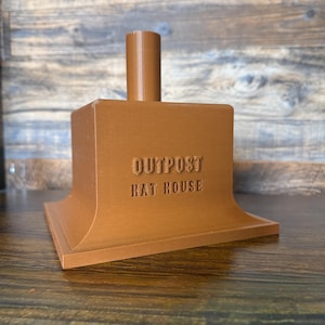 May include: A brown, 3D-printed hat stand with the text "OUTPOST HAT HOUSE" embossed on the front. The stand has a rectangular base with a flared design and a cylindrical post extending upwards.