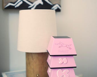 Puede incluir: Una pila de cuatro objetos de color rosa con forma trapezoidal y bordes negros. Las piezas superior e inferior muestran un dibujo lineal de un perro atrapando un disco y el texto Dog Sport Art Design. Las dos piezas centrales tienen un icono de hueso blanco.