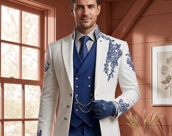 May include: A long white coat featuring blue floral embroidery on the lapels and cuffs, worn over a blue double-breasted waistcoat with a silver chain, a blue tie, a light shirt, blue trousers, and blue leather gloves, creating a formal ensemble.