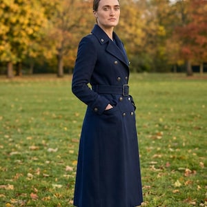 May include: A long, navy blue double-breasted wool coat featuring a structured collar, shoulder epaulets, and a matching fabric belt with a rectangular buckle. The coat has two side pockets and metallic buttons down the front and on the cuffs.