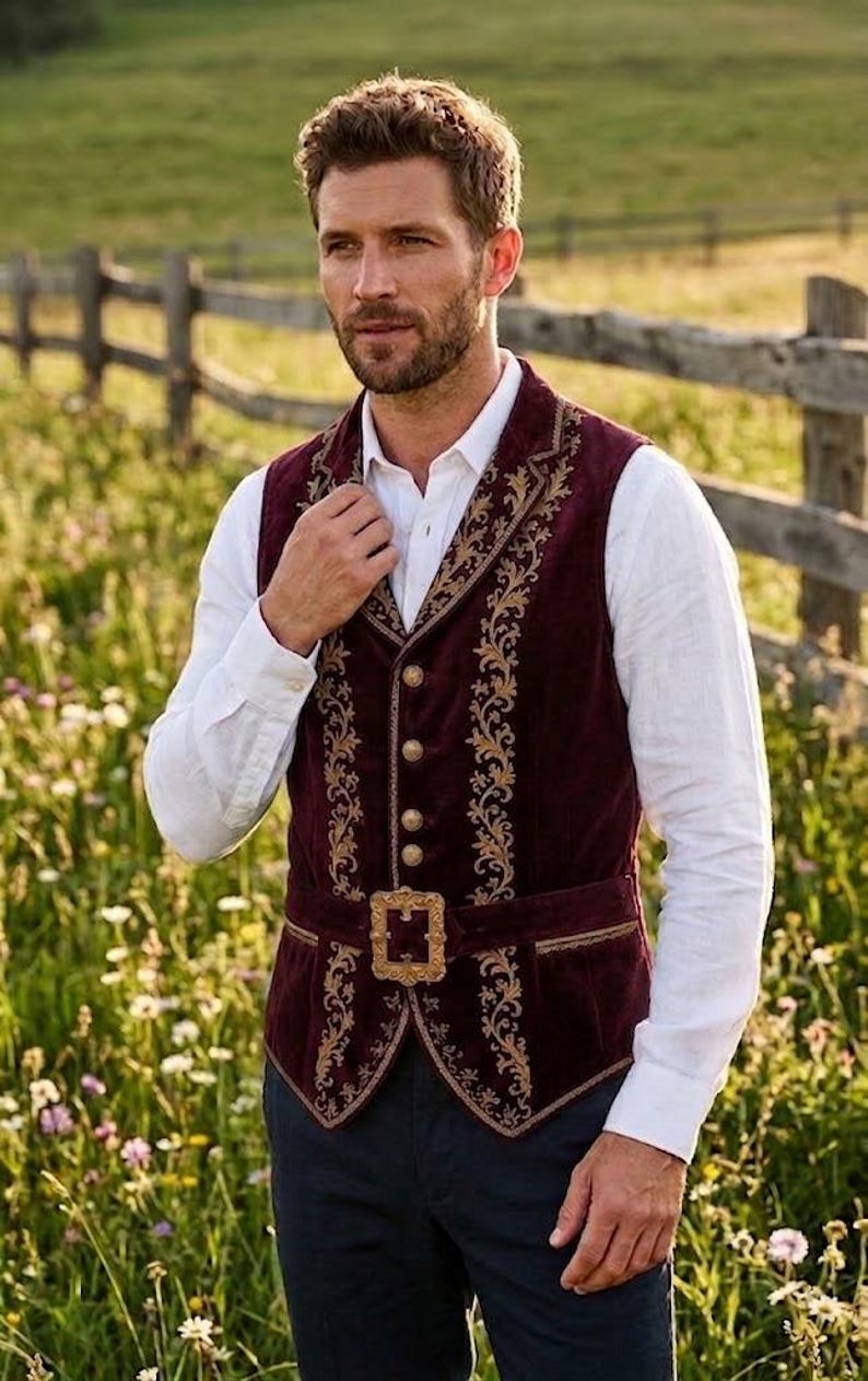 May include: A deep burgundy velvet vest featuring intricate gold floral embroidery along the lapels and front panels. The garment includes a row of round gold buttons and a matching gold buckle belt at the waist, worn over a white long-sleeve shirt.