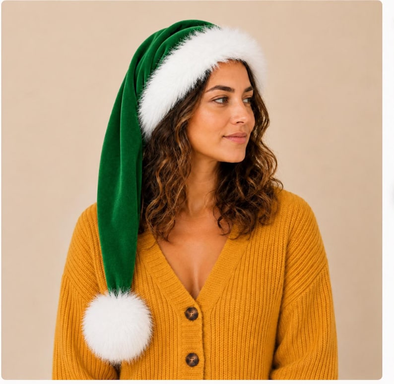 May include: A long, deep green velvet hat featuring a thick, fluffy white faux fur trim around the base and a large, round white faux fur pom-pom attached to the pointed tip. The hat is worn on the head, extending down to the shoulder.