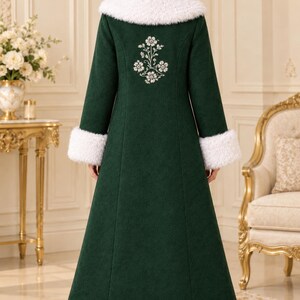 Pu&ograve; includere: Un cappotto lungo verde scuro con colletto e polsini in pelliccia sintetica bianca. Il retro del cappotto &egrave; decorato con ricami floreali bianchi tra le spalle e lungo l'orlo, rifinito con un'ampia fascia di pelliccia sintetica bianca.