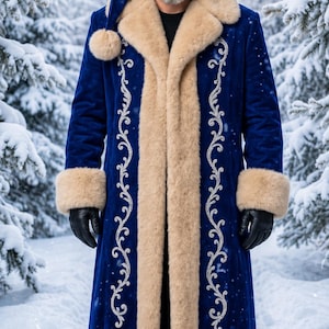 May include: A long, royal blue velvet coat featuring thick, cream-colored faux fur trim on the collar, cuffs, and hem. The coat is decorated with intricate silver embroidery along the front panels and is paired with a matching blue velvet hat.