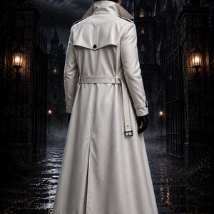 May include: A long, off-white trench coat featuring a wide collar, a back storm flap with a single button, a belted waist with a rectangular buckle, and adjustable cuffs. The coat is worn over dark clothing and black boots, viewed from the back.