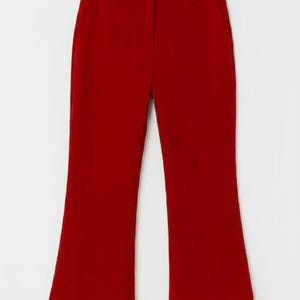 May include: A pair of solid red trousers featuring a straight-leg cut and a wide, plush white faux fur trim at the bottom of each leg. The trousers include a standard waistband with belt loops and a central zip fly, hanging from a black hanger.