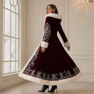 May include: A floor-length, deep burgundy velvet coat featuring a white faux fur trim along the hood, cuffs, and hem. The coat is adorned with intricate silver floral embroidery patterns along the sleeves and the lower section of the skirt.