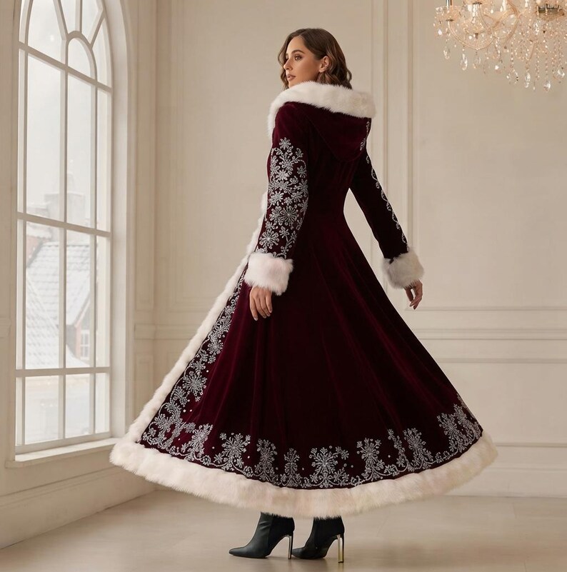 May include: A floor-length, deep burgundy velvet coat featuring a white faux fur trim along the hood, cuffs, and hem. The coat is adorned with intricate silver floral embroidery patterns along the sleeves and the lower section of the skirt.