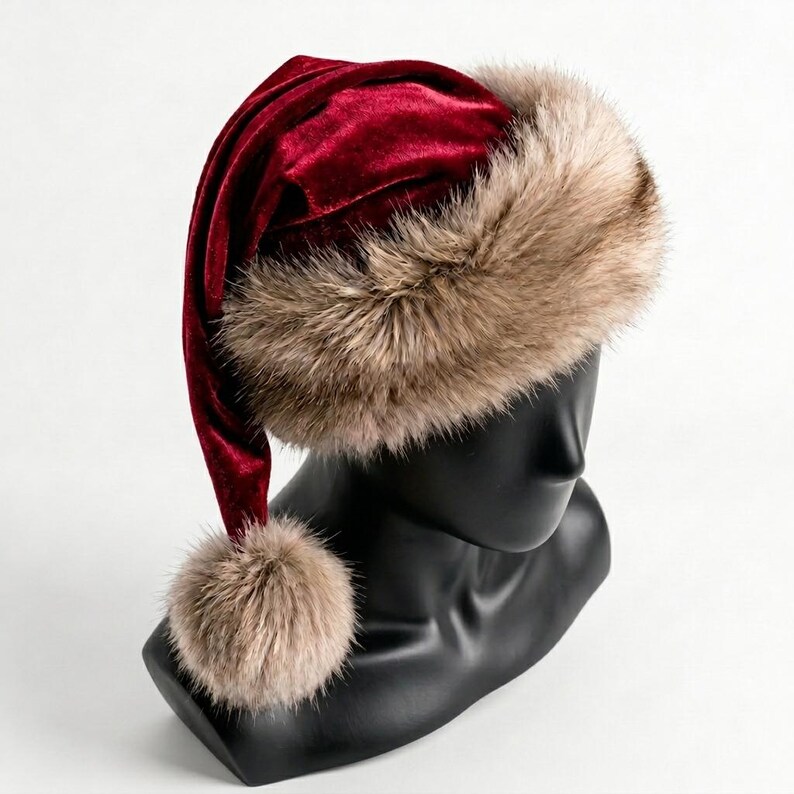 Puede incluir: Un gorro de terciopelo rojo intenso con una banda ancha y gruesa de piel sint&eacute;tica de color marr&oacute;n claro en la base. El gorro tiene una punta larga que cae hacia un lado, rematada con un pomp&oacute;n de piel sint&eacute;tica a juego.