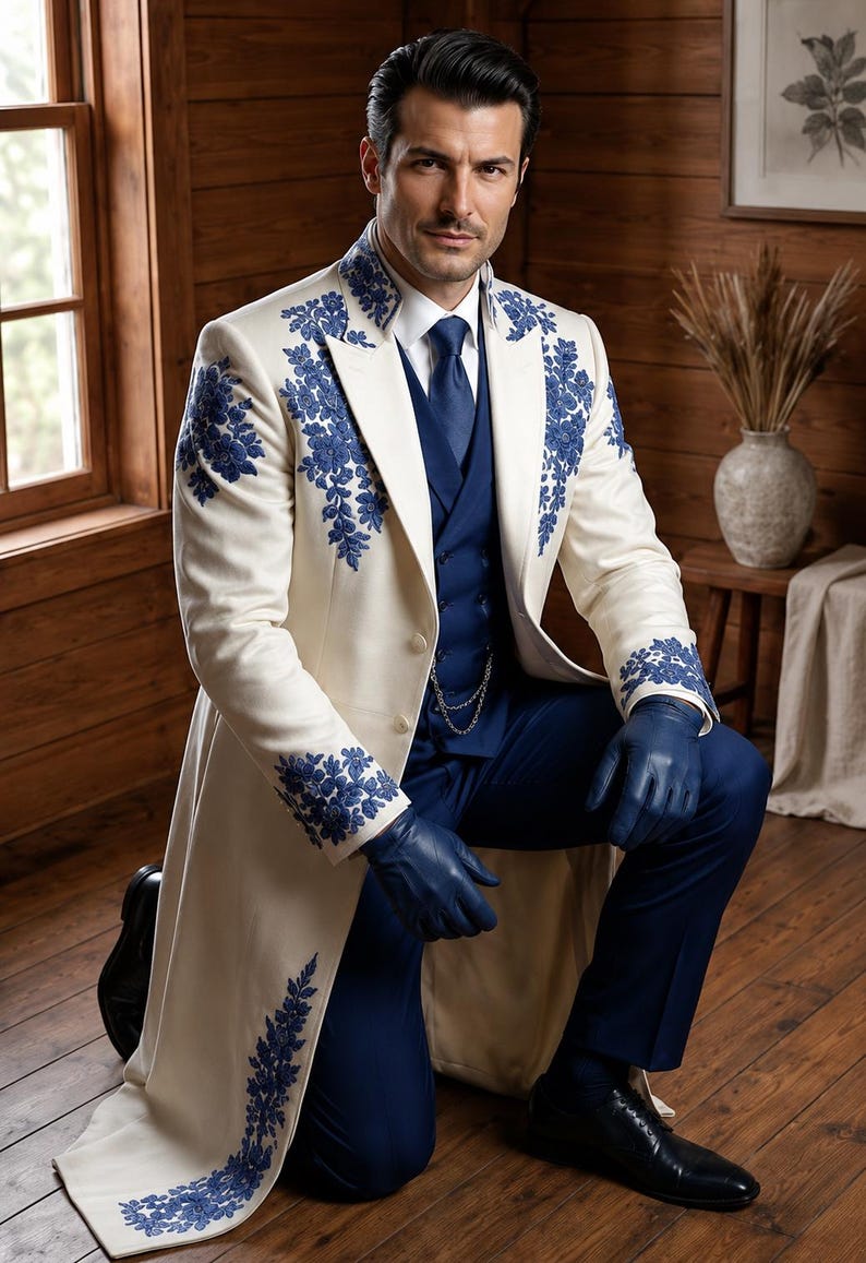 Puede incluir: Un abrigo largo de color crema con intrincados bordados florales azules en las solapas, los hombros y los pu&ntilde;os. El abrigo se lleva sobre un chaleco azul oscuro, una camisa blanca de cuello, una corbata azul, pantalones azul oscuro y guantes de cuero azul.