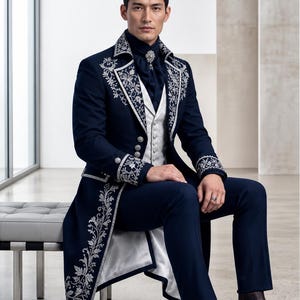 Puede incluir: Una levita azul marino oscuro con bordados florales plateados en solapas y pu&ntilde;os, combinada con un chaleco plateado estampado, camisa azul marino con broche plateado, pantalones a juego y botas de cuero en tono marr&oacute;n oscuro.