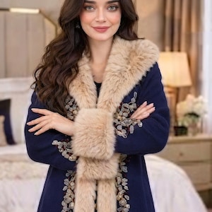 May include: A navy blue coat featuring a thick beige faux fur collar and cuffs. The front of the coat is decorated with intricate floral embroidery in shades of gold, silver, and deep red, extending along the edges of the fur trim.