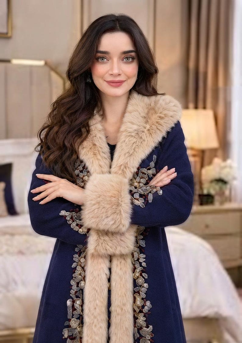 May include: A navy blue coat featuring a thick beige faux fur collar and cuffs. The front of the coat is decorated with intricate floral embroidery in shades of gold, silver, and deep red, extending along the edges of the fur trim.