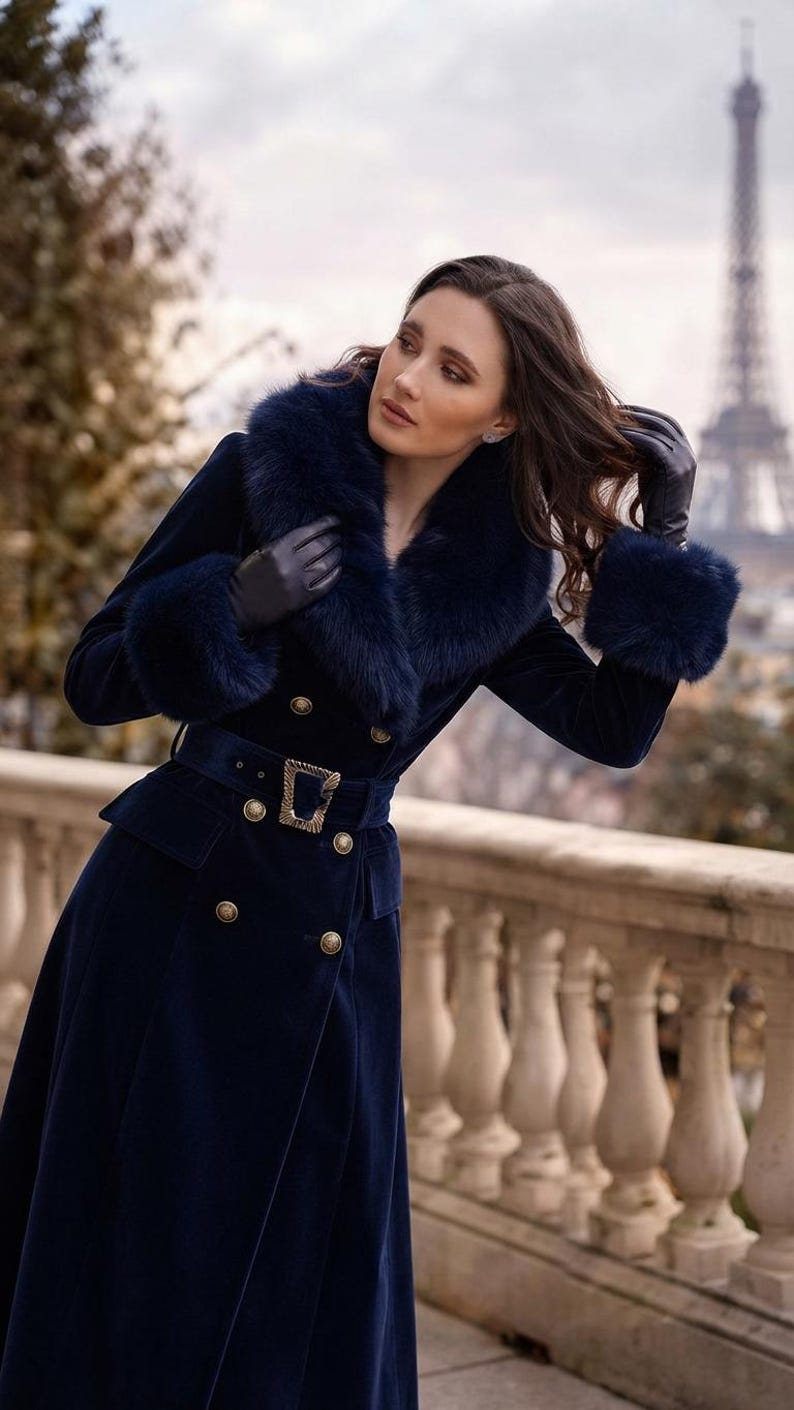 May include: A long, dark blue velvet coat featuring a wide faux fur collar and matching faux fur cuffs. The coat is double-breasted with gold-toned buttons, a belted waist with a rectangular gold buckle, and two flap pockets at the hips.