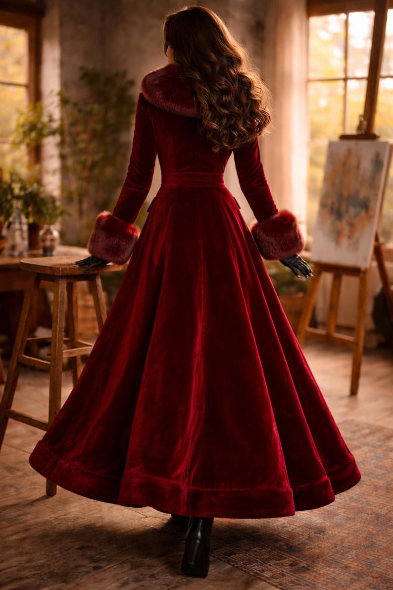 May include: A floor-length, deep red velvet coat featuring a wide, plush faux fur collar and matching faux fur cuffs on the long sleeves. The coat has a fitted bodice with a defined waistline and a full, flared skirt that reaches the floor.