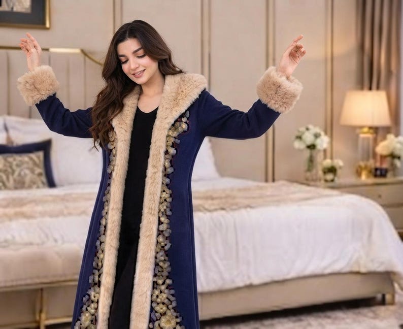 May include: A long, navy blue coat featuring a thick, beige faux fur trim along the hood, front opening, and sleeve cuffs. The coat is decorated with a vertical floral embroidery pattern in gold and blue tones along the front edges.